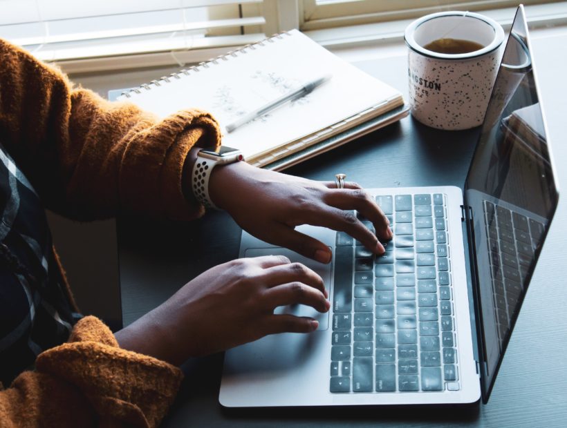 Black woman typing on her laptop with documents and coffee beside her